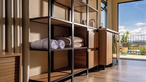 A hotel room with a wooden floor, a built-in shelf with towels, a wooden cabinet, and a large window offering a view of the outdoors. - Hotel Mito Guatapé (Guatapé)