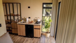A compact kitchen with a sink, stove, and wooden cabinets. A potted plant is visible near the window, and a black refrigerator is present. - Hotel Mito Guatapé (Guatapé)