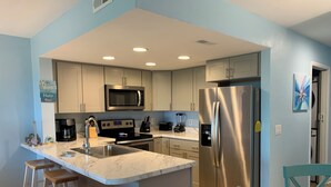 A modern kitchen with a central island, stainless steel appliances, and light blue cabinetry. - Beach Lovers, Oceanview, Cute 1 BR, 2 full BA condo in Surf City sleeps 5 (Surf City)