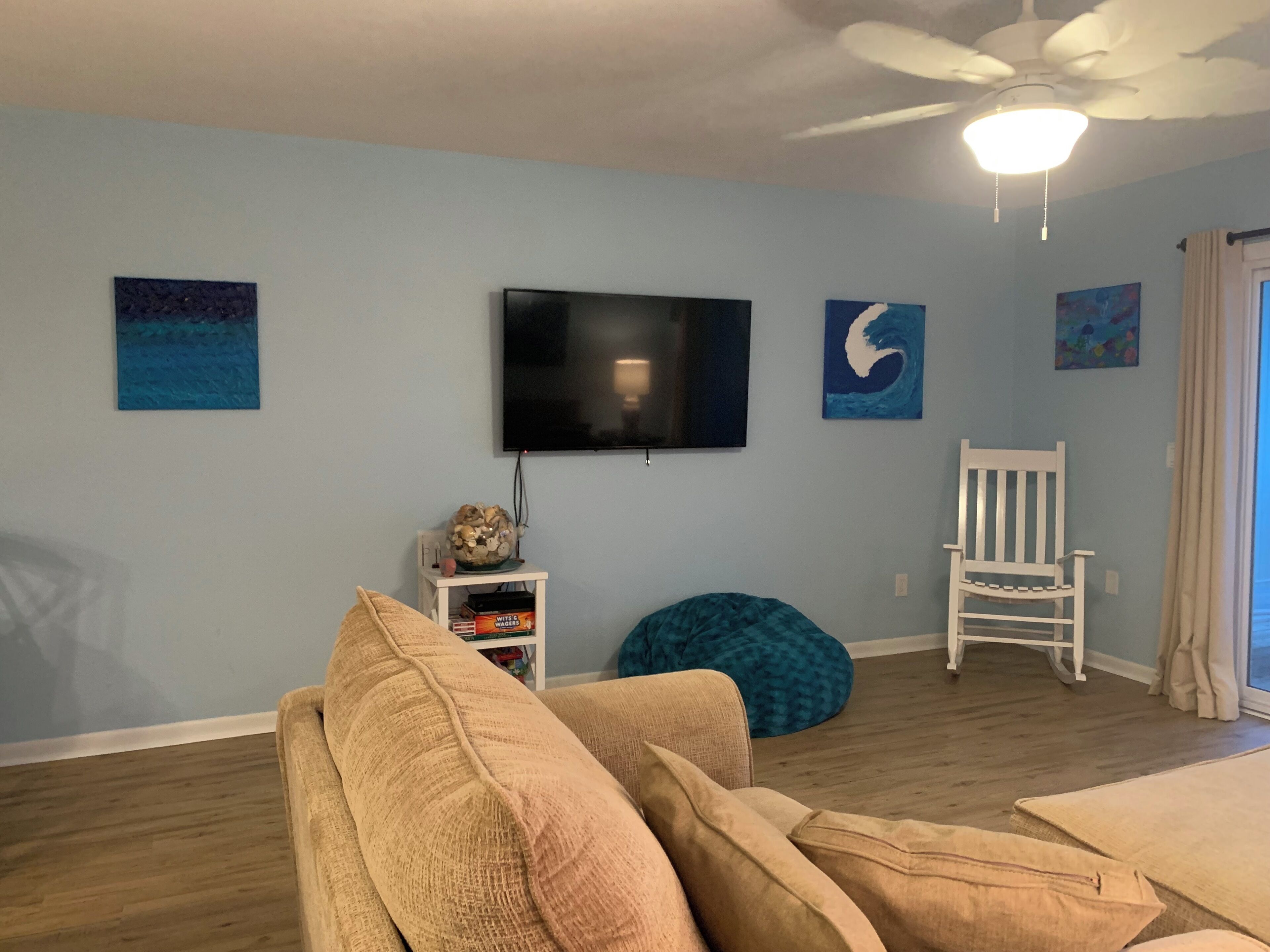 A living room with a ceiling fan, a flat-screen TV, and a white chair.