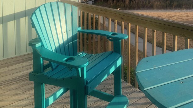A wooden deck with a turquoise Adirondack chair and a matching table. A wooden railing and a view of the ocean and beach are visible. - Beach Lovers, Oceanview, Cute 1 BR, 2 full BA condo in Surf City sleeps 5 (Surf City)