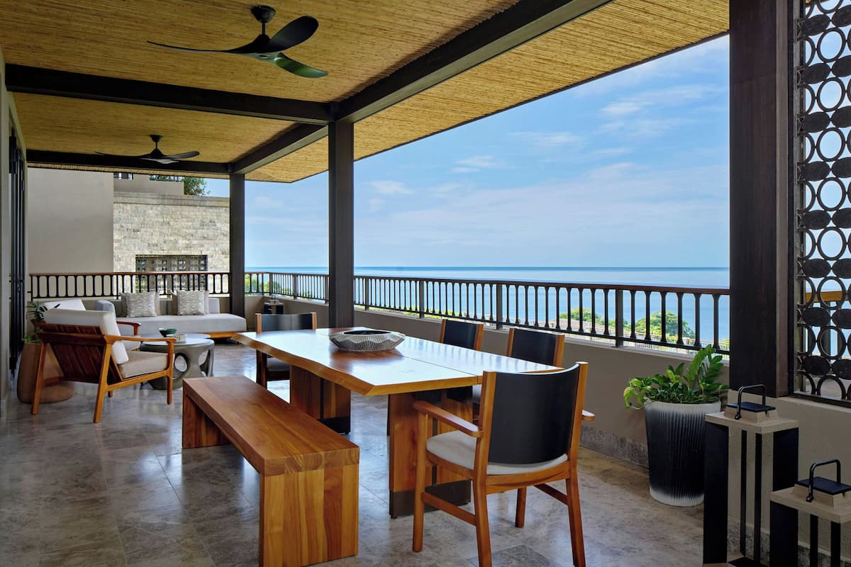 A spacious balcony with a wooden table and chairs, a sofa, and a potted plant.
