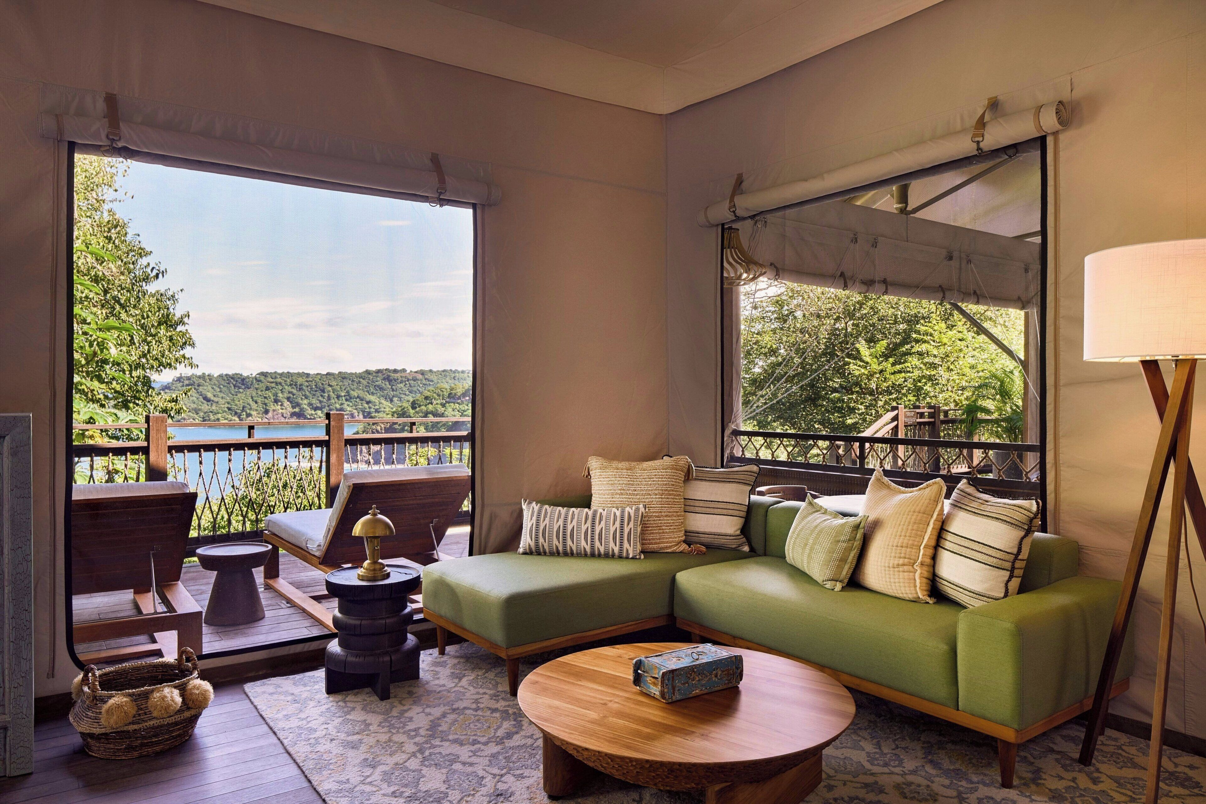 A cozy lounge area with a green sofa, a round wooden table, and a view of a lush landscape.