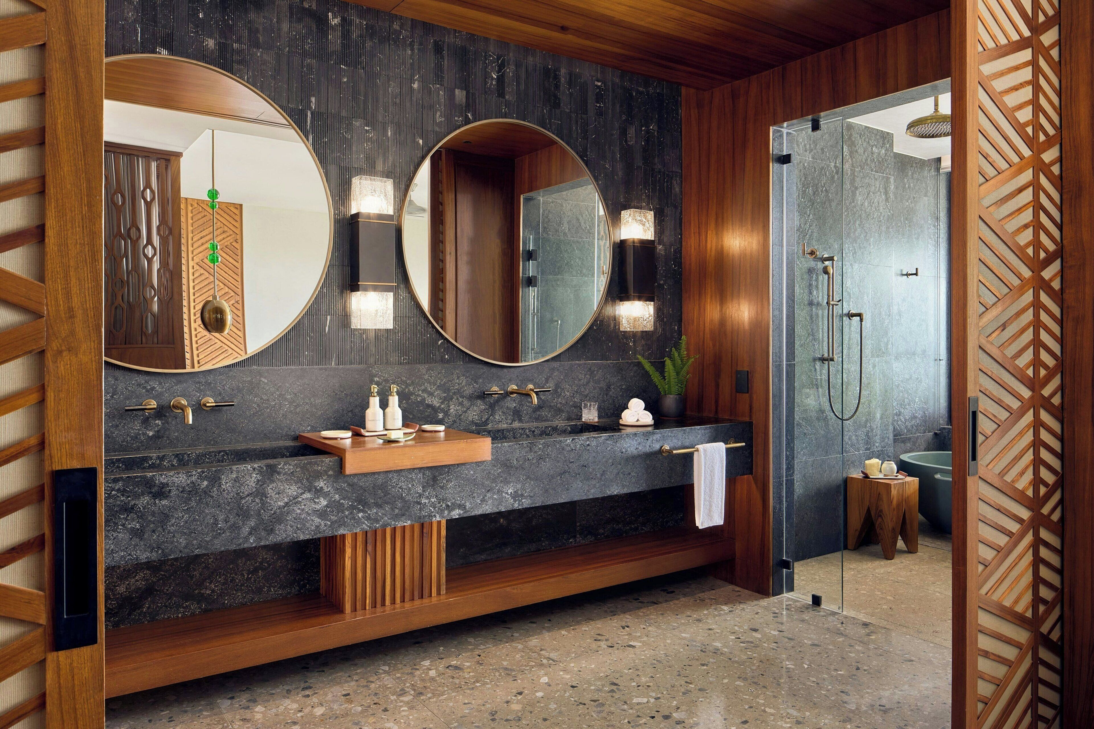A modern bathroom with a wooden vanity, two large mirrors, a built-in shower, and a small wooden stool.