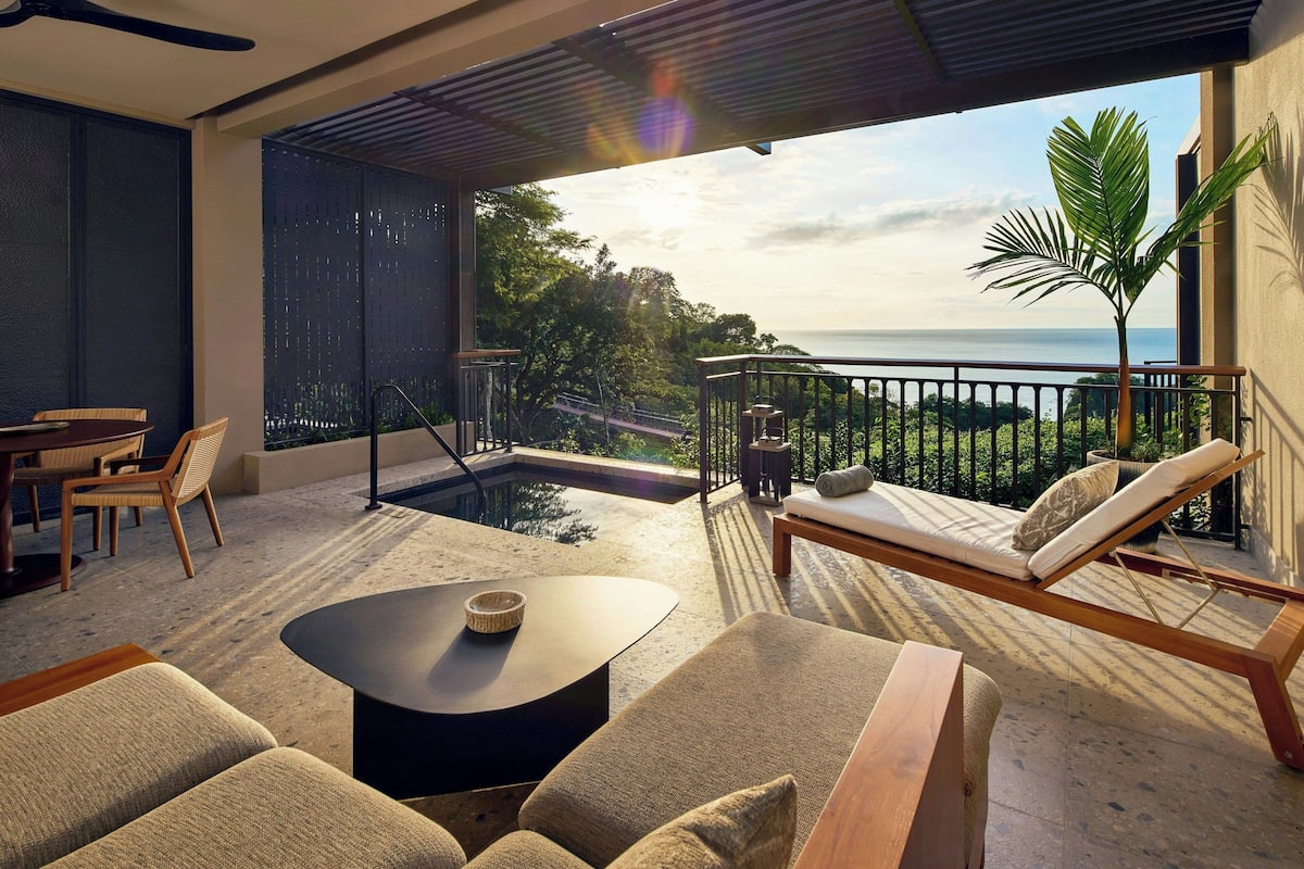A modern outdoor lounge area with a pool, seating, and a view of the ocean.