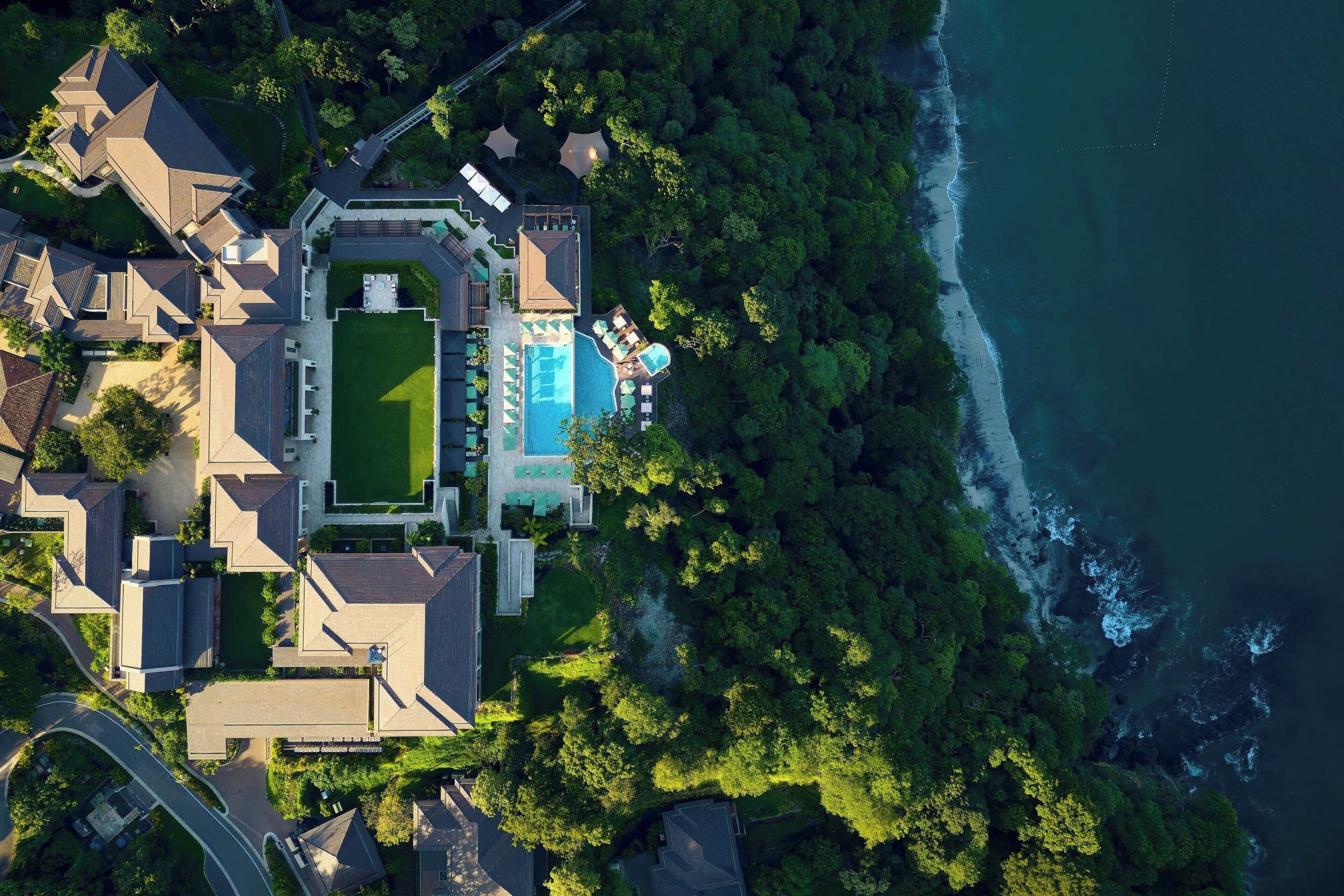 Vue aérienne d’une propriété située sur la côte, avec une piscine, plusieurs bâtiments et une végétation luxuriante.