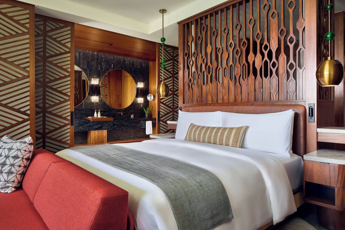 A hotel room with a large bed, a red sofa, a wooden partition, and a circular mirror.