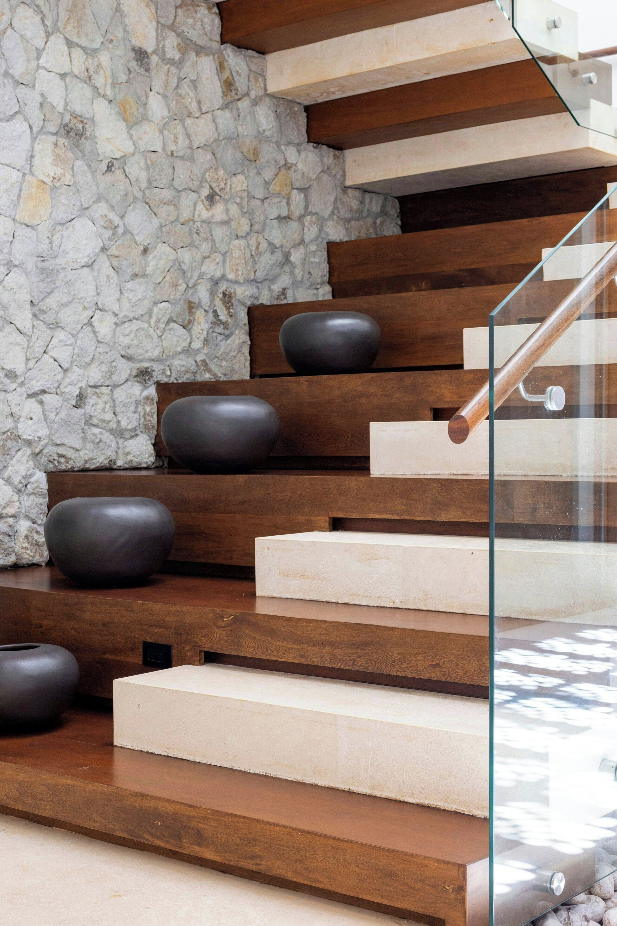 Una escalera de madera con barandilla de vidrio que lleva a un muro de piedra.