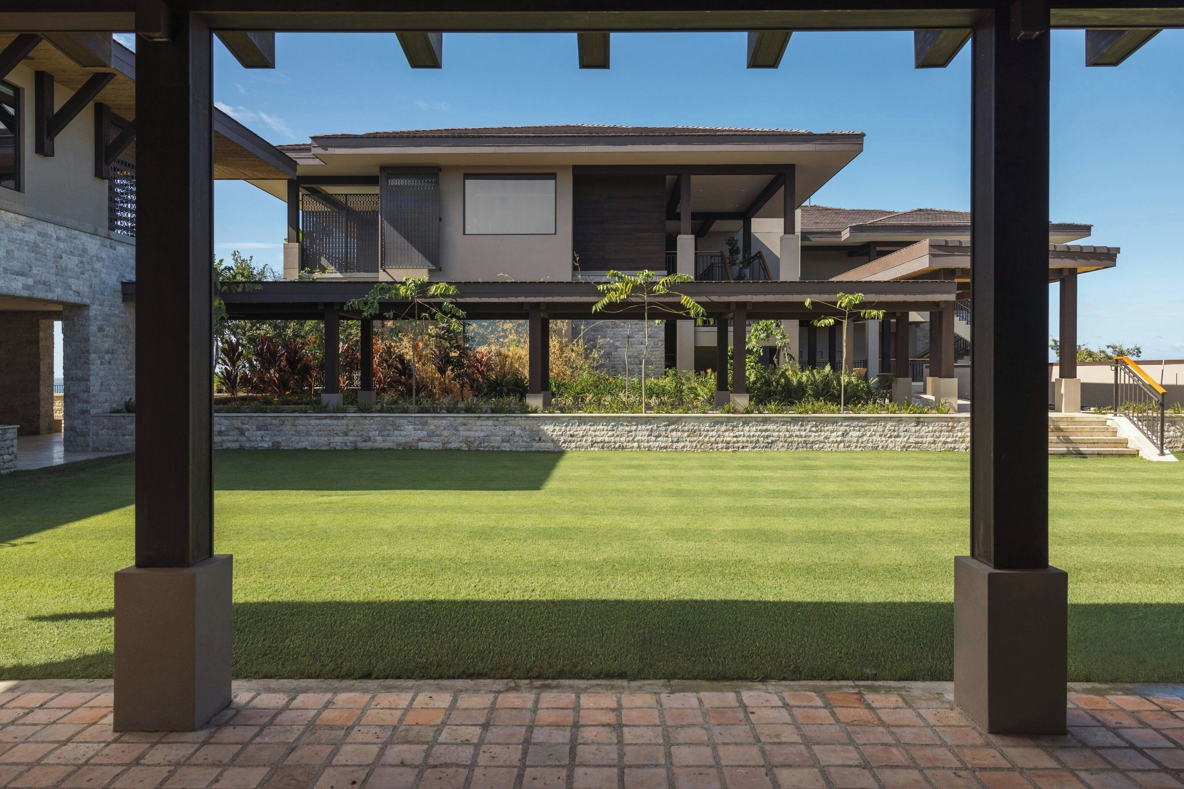 Une maison moderne dotée d’un patio couvert, d’une pelouse bien entretenue et d’un mur de soutènement en pierre.