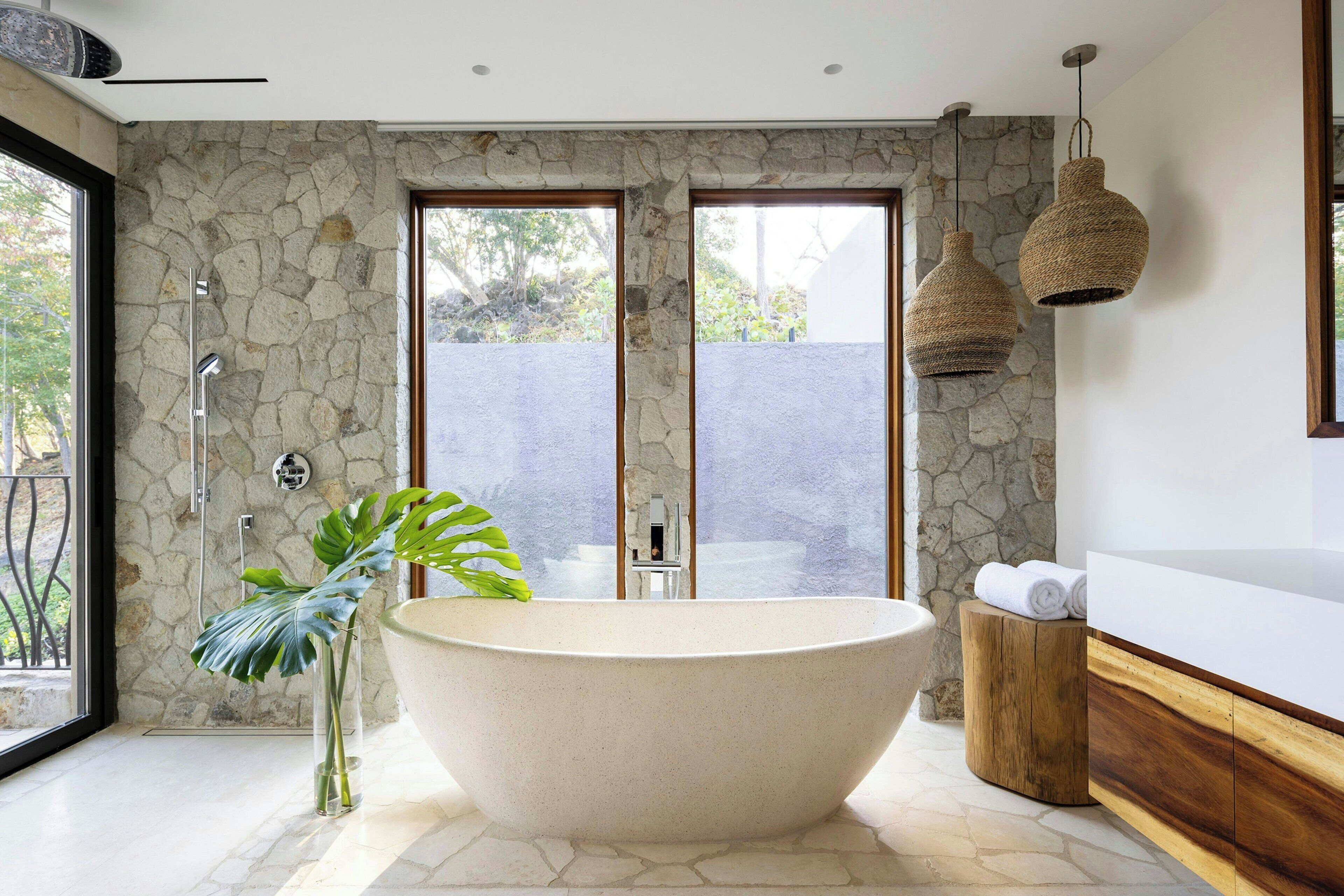 Un baño moderno con una bañera independiente, un tocador de madera y una pared de piedra.