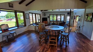 Une pièce spacieuse avec une grande table ronde et des chaises en bois, un téléviseur et une vue sur l’extérieur.