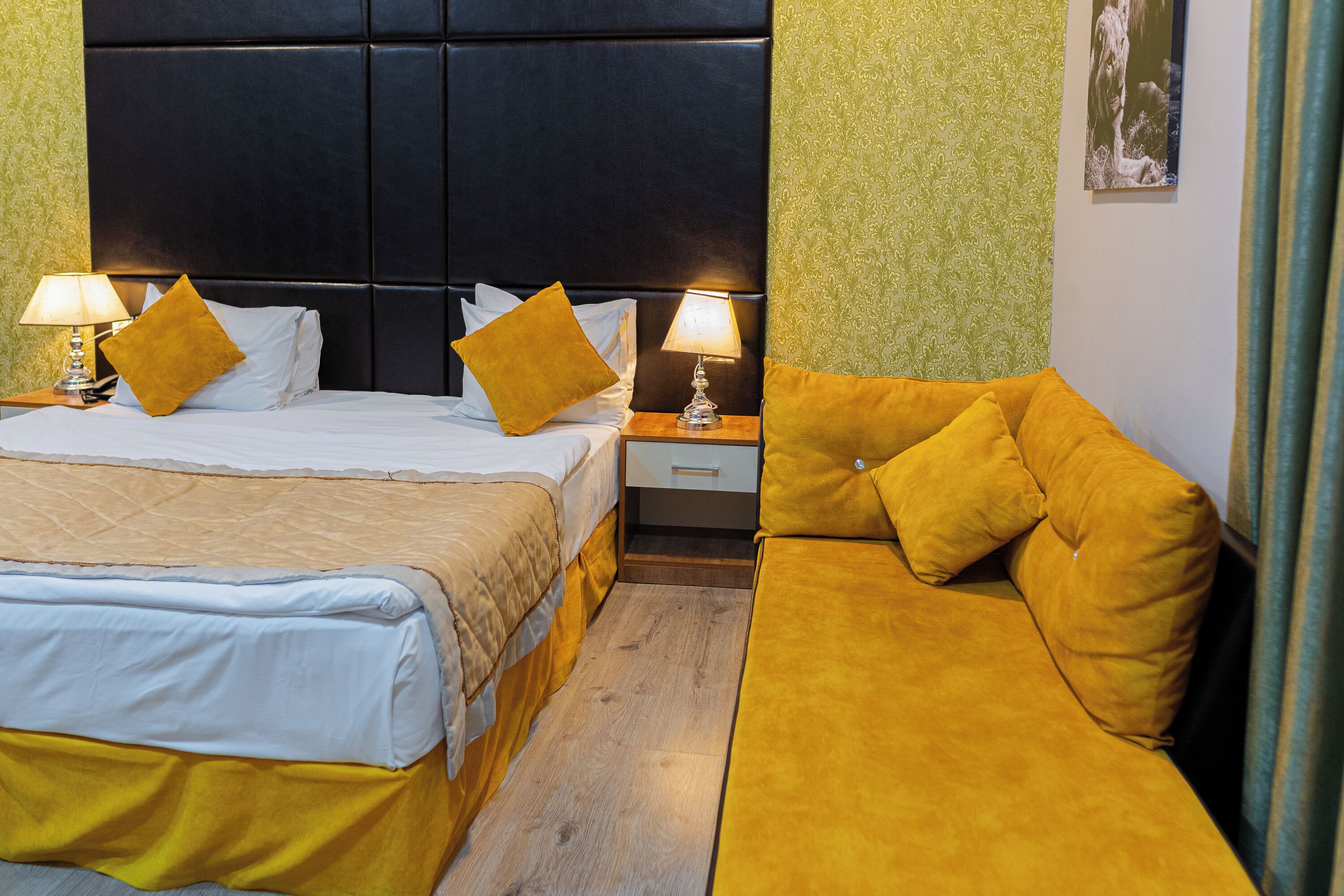 A hotel room with a large bed, a sofa, two nightstands with lamps, and a headboard.