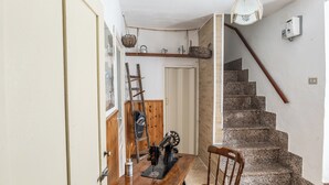 A kitchen with a wooden table, a sewing machine, and a chair. There is a staircase with a wooden handrail and a wall-mounted light fixture. - Casa Della Nonna (Sperlinga)