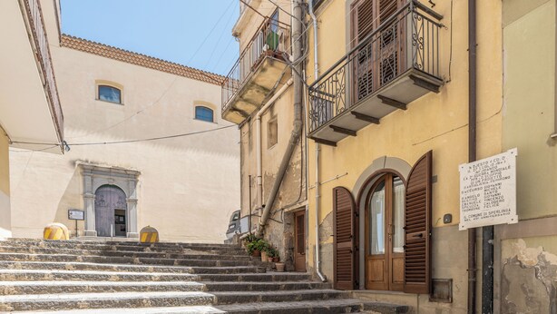 A narrow street with stone steps leading to a building with a wooden door and a balcony. - Casa Del Sarto (Sperlinga)