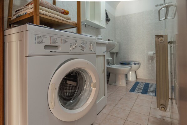 A compact laundry room with a front-loading washing machine, a toilet, and a shower area. - Casa Del Sarto (Sperlinga)