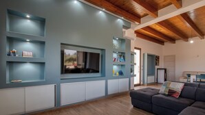A modern living room with a large TV, built-in shelves, a sofa, and a wooden ceiling. - Villa Ginevra (Santa Ninfa)