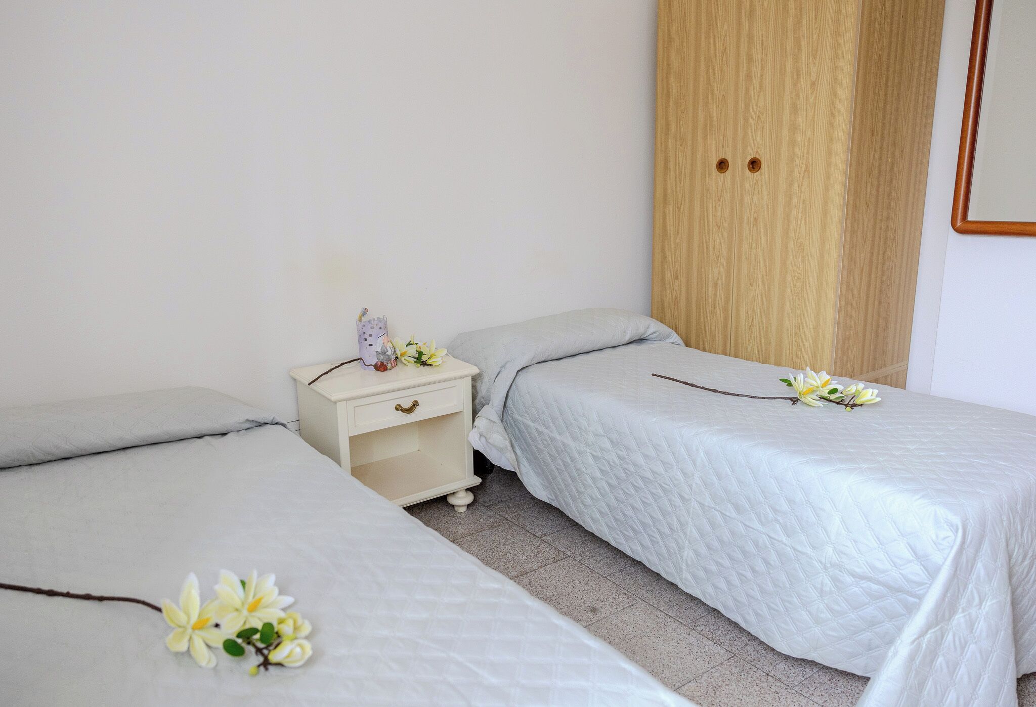 Un dormitorio con dos camas, un armario de madera y una mesita de noche con una lámpara y flores.