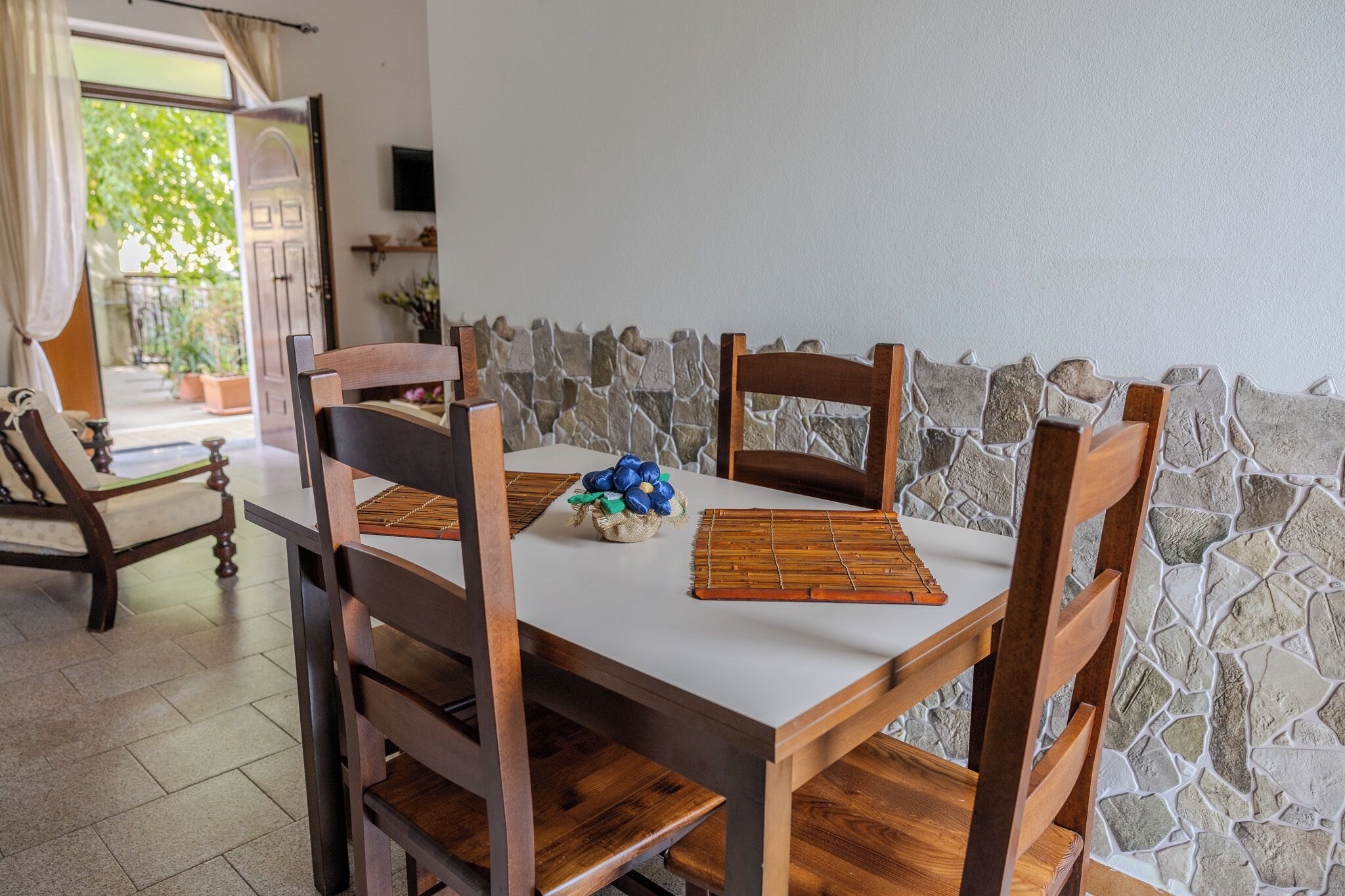 Un comedor con una mesa blanca, sillas de madera, una pared de piedra y vistas al exterior.