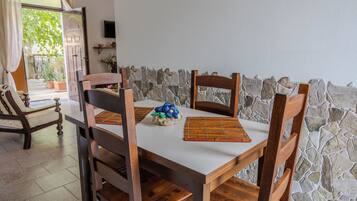 Un comedor con una mesa blanca, sillas de madera, una pared de piedra y vistas al exterior.