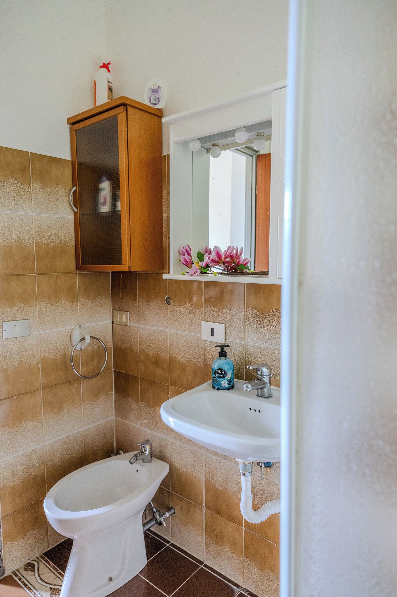A bathroom with a white toilet, a white sink, and a wooden cabinet above the sink.