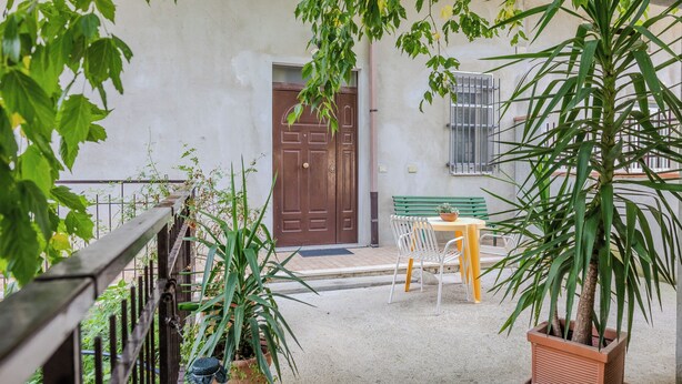 A courtyard with a wooden door, a bench, a table, and potted plants. - Casa Vacanza Mary (Guardavalle)