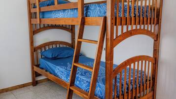 Una cama litera con escalera de madera, ropa de cama azul estampada y una pared blanca al fondo.