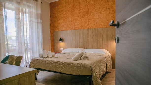 A hotel room with a bed, a desk, a chair, and a window with sheer curtains.