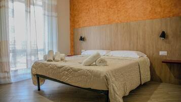 Un letto rifatto con una coperta beige, due cuscini e asciugamani arrotolati su un pavimento in legno.