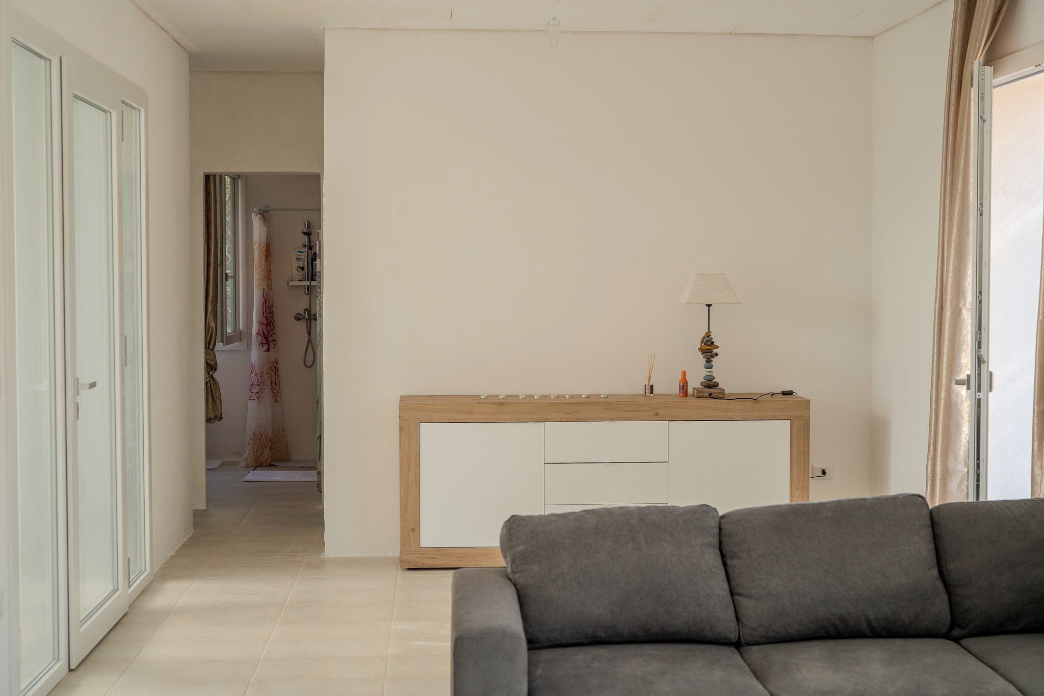 Un salon moderne avec un canapé gris, une console en bois surmontée d’une lampe et un meuble blanc.