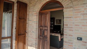 A brick building with a wooden door and an arched doorway leading to a room with a sofa and a television. - A Casa Di Lea (Mondavio)