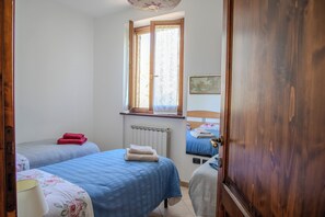 A bedroom with two beds, a window, a radiator, and a wooden door. - A Casa Di Lea (Mondavio)