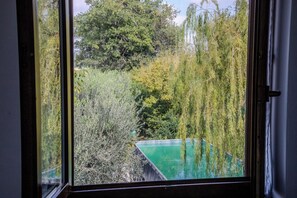 A view through a window of a swimming pool surrounded by dense foliage and trees. - A Casa Di Lea (Mondavio)