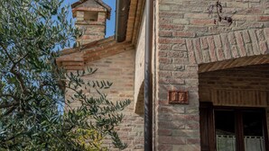 A rustic stone building with a brick chimney, a small window with shutters, and a visible number plaque. - A Casa Di Lea (Mondavio)