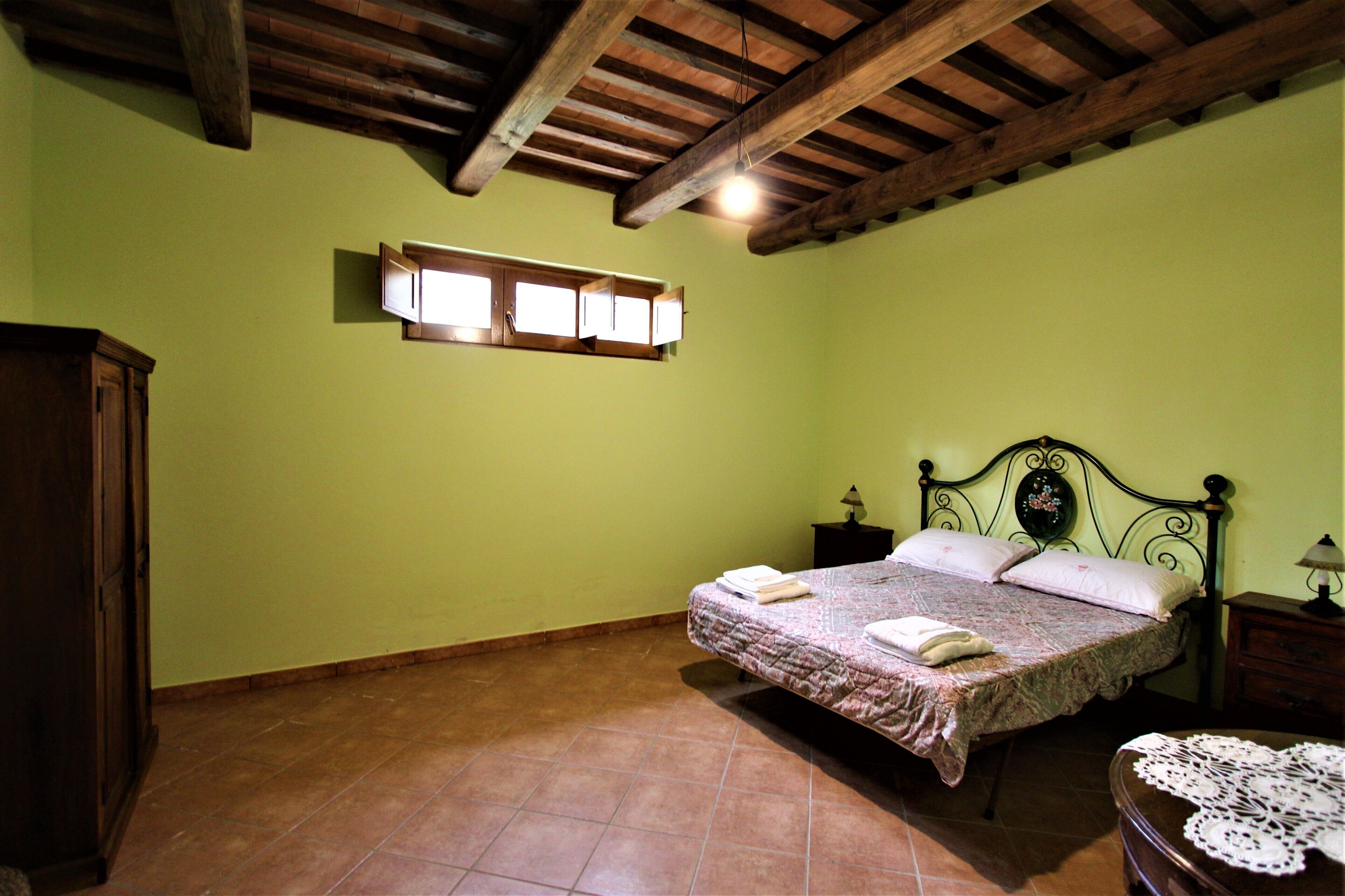A bedroom with a bed, a nightstand, a wooden wardrobe, and a window with lights.
