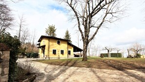 Un edificio amarillo con base de piedra, un porche cubierto y un gran árbol en la parte delantera.