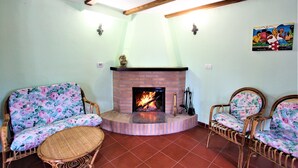Una sala de estar con chimenea de ladrillo, dos sofás de mimbre con tapicería floral y una pequeña mesa redonda.