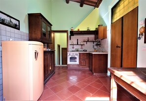 Eine Küche mit Kühlschrank, Herd, Backofen, Holzschränken und gefliestem Boden.
