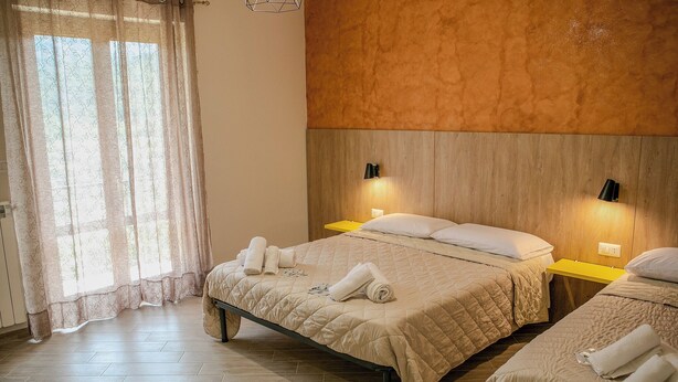 Camera d'albergo con due letti, una testiera in legno, lampade sui comodini e una finestra con tende.