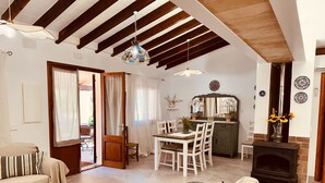 Un salon chaleureux avec un canapé, une table basse en bois, un coin repas avec une table et des chaises, une cheminée et un coin cuisine équipé d’une cuisinière et de placards.