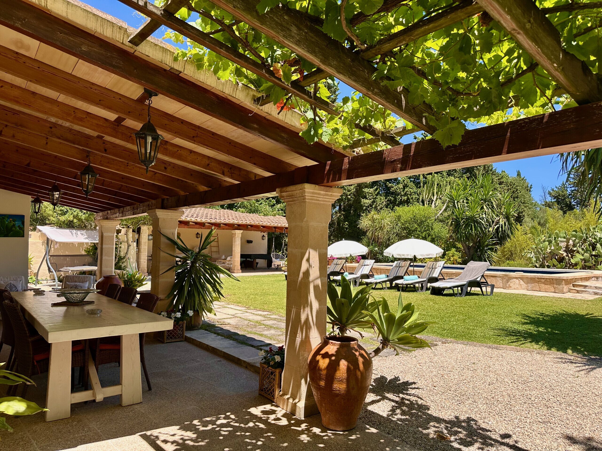 Une terrasse extérieure dotée d’une pergola, d’une table avec des chaises et d’un espace piscine avec des chaises longues.