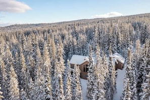 A cabin surrounded by dense, snow-covered forest. - Lovely renovated home w/ hot tub & stunning views (Big Sky)