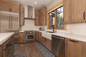 A kitchen with wooden cabinets, stainless steel appliances, a window with a view, and a marble countertop.