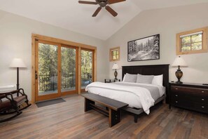 A bedroom with a bed, a bench, a dresser, a ceiling fan, and a large window with a view of trees.