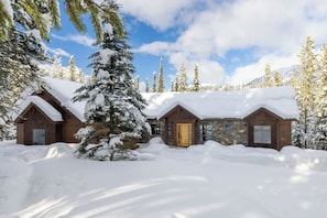 A snow-covered lodge with multiple cabins, surrounded by evergreen trees and a clear sky.
