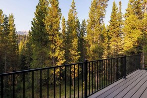 A wooden deck with a black railing overlooking a forest of tall evergreen trees. - Lovely renovated home w/ hot tub & stunning views (Big Sky)