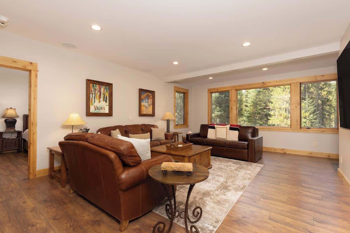 A spacious living room with leather sofas, a coffee table, and large windows offering a view of trees.