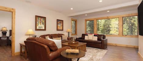 A spacious living room with leather sofas, a coffee table, and large windows offering a view of trees.