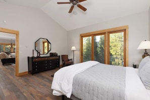 A bedroom with a bed, dresser, chair, and a balcony with a view. - Lovely renovated home w/ hot tub & stunning views (Big Sky)
