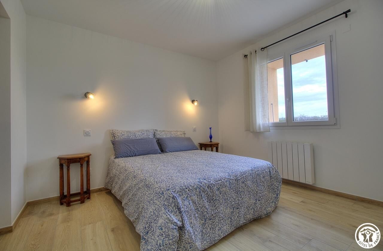 A bedroom with a bed, two bedside tables, a window with curtains, and a radiator.