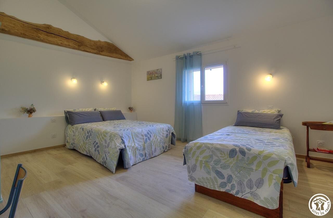 Une chambre avec deux lits, un plafond en bois, une fenêtre avec des rideaux et des lampes fixées au mur.